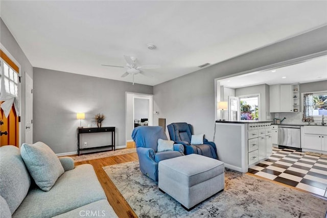 living room with light floors, baseboards, visible vents, and ceiling fan