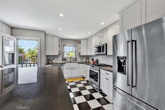 kitchen with dark floors, a sink, appliances with stainless steel finishes, open shelves, and tasteful backsplash