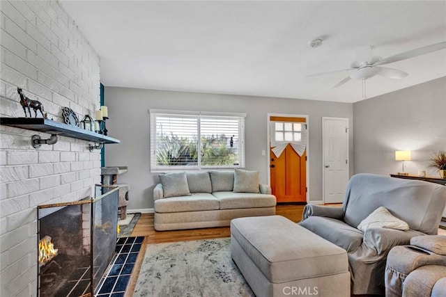 living area featuring a brick fireplace, baseboards, a ceiling fan, and wood finished floors