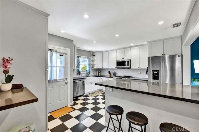 kitchen featuring light floors, a breakfast bar area, stainless steel appliances, dark countertops, and visible vents