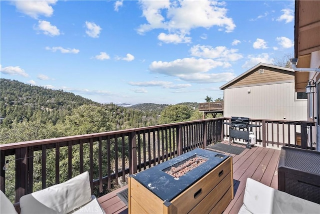 deck with an outdoor fire pit, a view of trees, and grilling area