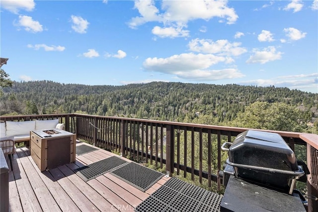 wooden deck featuring a forest view, a grill, and an outdoor fire pit