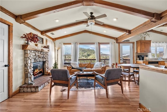 living room with lofted ceiling with beams, light wood-style flooring, ceiling fan, and a stone fireplace