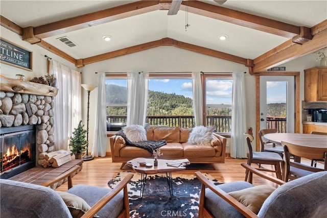 living area featuring lofted ceiling with beams, a stone fireplace, visible vents, and light wood-style floors