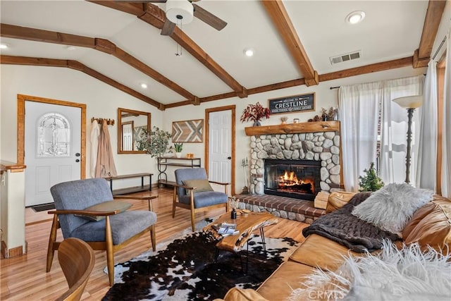 living room featuring a stone fireplace, visible vents, lofted ceiling with beams, and wood finished floors