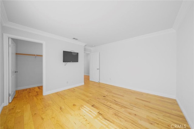 unfurnished bedroom featuring visible vents, baseboards, a spacious closet, ornamental molding, and light wood-type flooring