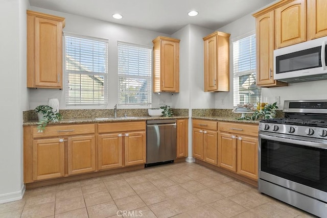 kitchen with dark stone countertops, stainless steel appliances, light brown cabinets, a sink, and recessed lighting