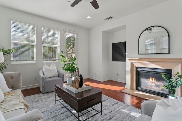 living room with a glass covered fireplace, wood finished floors, visible vents, and baseboards