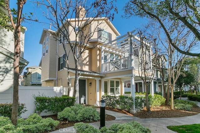 view of front of property with fence, a chimney, and a balcony