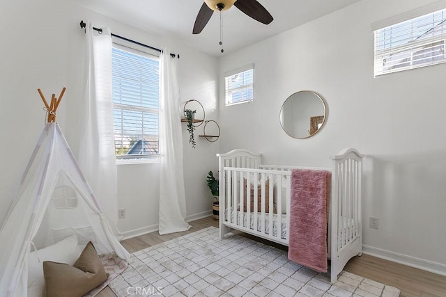 bedroom featuring light wood finished floors, a crib, a ceiling fan, and baseboards