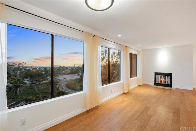 unfurnished living room featuring wood finished floors, a fireplace with flush hearth, and a wealth of natural light