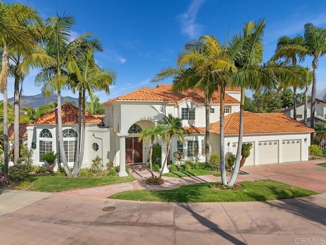 mediterranean / spanish house featuring driveway, an attached garage, a tile roof, and stucco siding