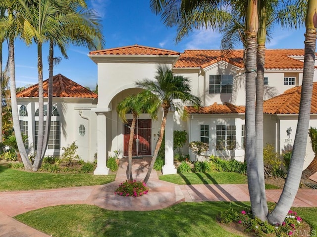 mediterranean / spanish house featuring a front lawn, a tile roof, and stucco siding