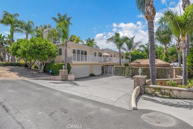 view of front of property with driveway, a garage, fence, a balcony, and stucco siding