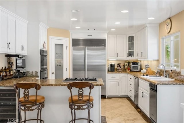 kitchen featuring appliances with stainless steel finishes, a sink, white cabinets, stone countertops, and a peninsula
