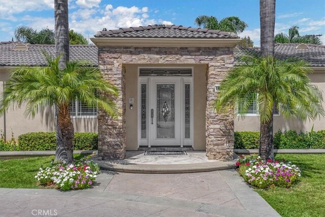 view of exterior entry with stucco siding, a tile roof, and stone siding