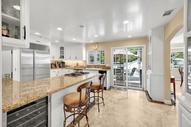 kitchen featuring light stone counters, appliances with stainless steel finishes, a sink, wine cooler, and visible vents