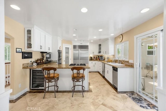kitchen featuring a sink, stone countertops, stainless steel appliances, a peninsula, and wine cooler