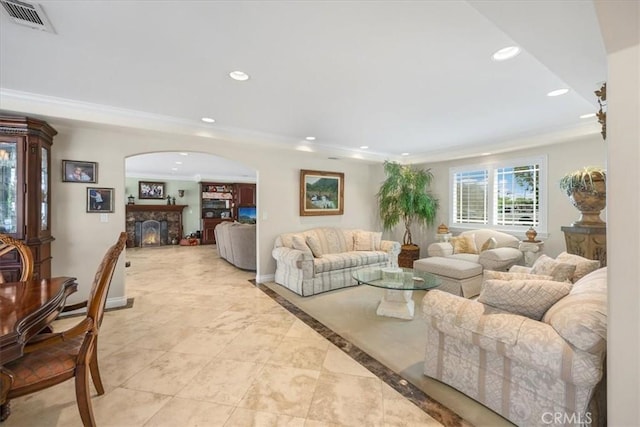 living room featuring visible vents, ornamental molding, a stone fireplace, recessed lighting, and arched walkways