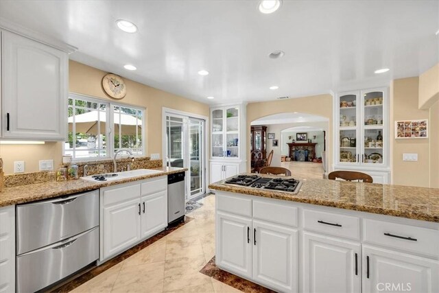 kitchen with white cabinets, appliances with stainless steel finishes, a sink, arched walkways, and glass insert cabinets