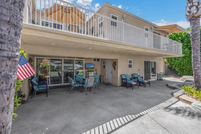 back of property featuring outdoor dining area, a patio, stucco siding, and a balcony