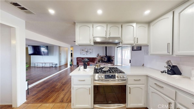 kitchen with under cabinet range hood, visible vents, gas range, and white cabinets