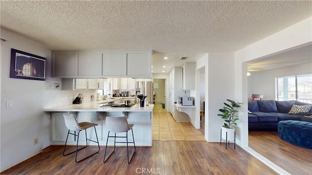 kitchen with a breakfast bar area, wood finished floors, a peninsula, light countertops, and white cabinets