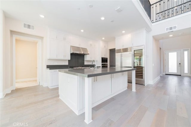 kitchen with stainless steel built in fridge, dark countertops, visible vents, and under cabinet range hood