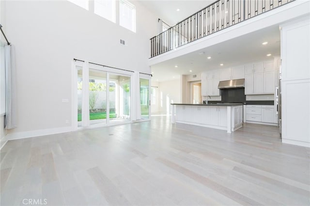 unfurnished living room with baseboards, recessed lighting, a sink, and light wood-style floors