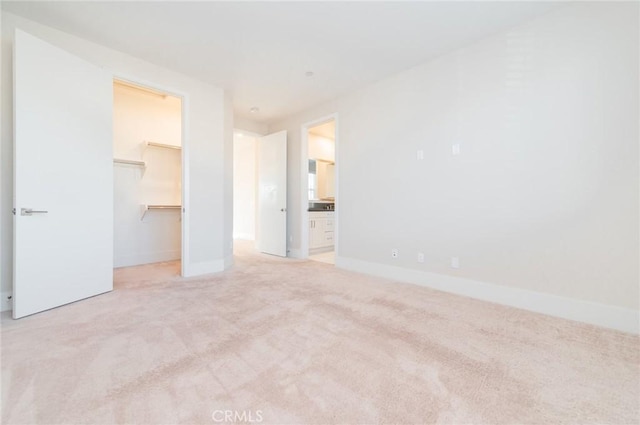 unfurnished bedroom featuring a walk in closet, a closet, carpet flooring, connected bathroom, and baseboards