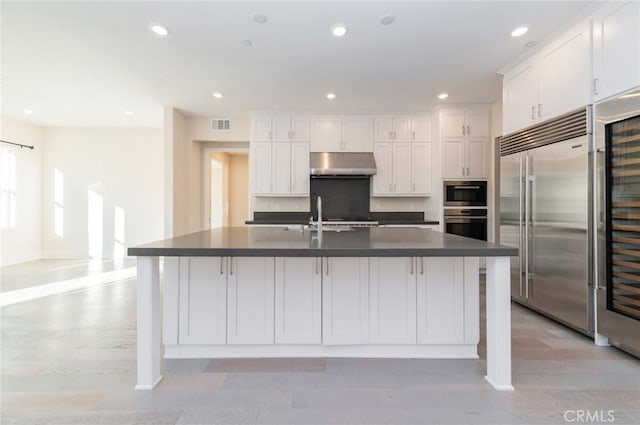 kitchen with appliances with stainless steel finishes, dark countertops, white cabinetry, and under cabinet range hood