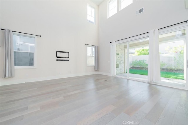 unfurnished living room featuring baseboards, a high ceiling, visible vents, and wood finished floors