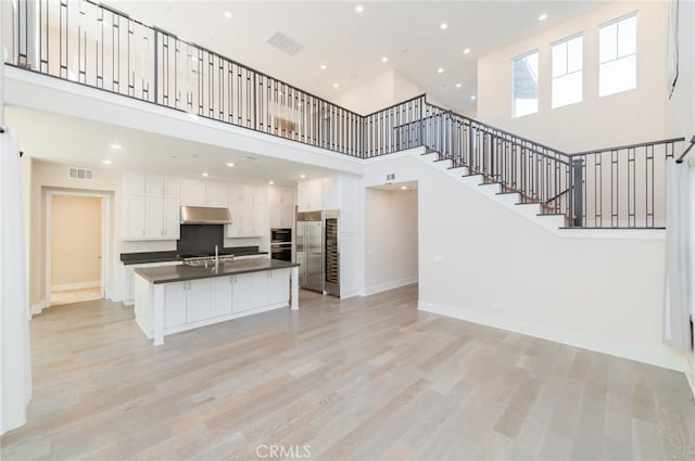 unfurnished living room featuring light wood-style floors, baseboards, stairway, and visible vents