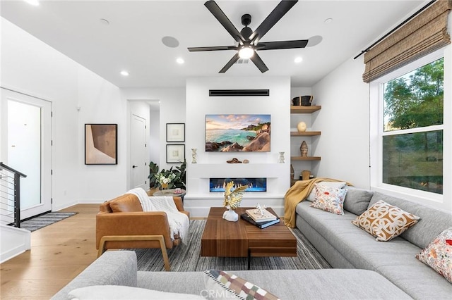 living area featuring baseboards, a glass covered fireplace, ceiling fan, wood finished floors, and recessed lighting