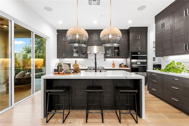 kitchen with under cabinet range hood, double wall oven, a breakfast bar area, and light countertops