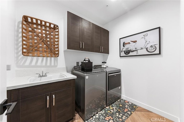 clothes washing area with independent washer and dryer, a sink, cabinet space, and baseboards