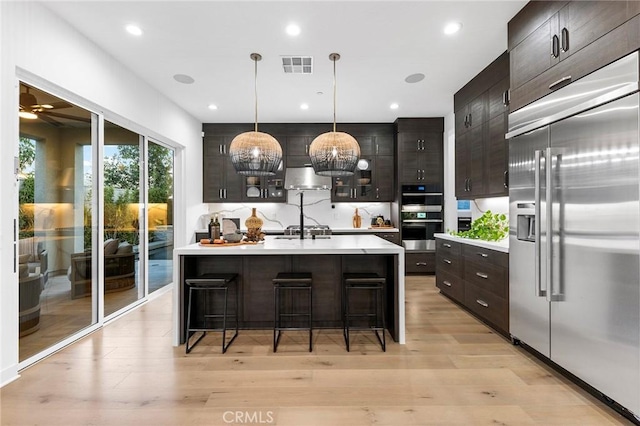 kitchen featuring stainless steel appliances, light countertops, visible vents, light wood-style floors, and a kitchen breakfast bar