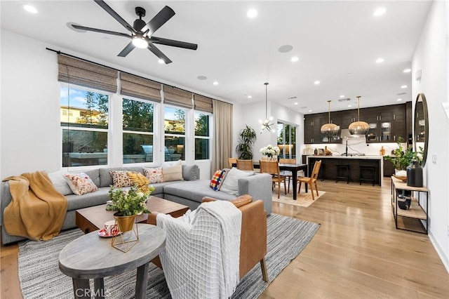 living room with ceiling fan with notable chandelier, light wood-style flooring, and recessed lighting