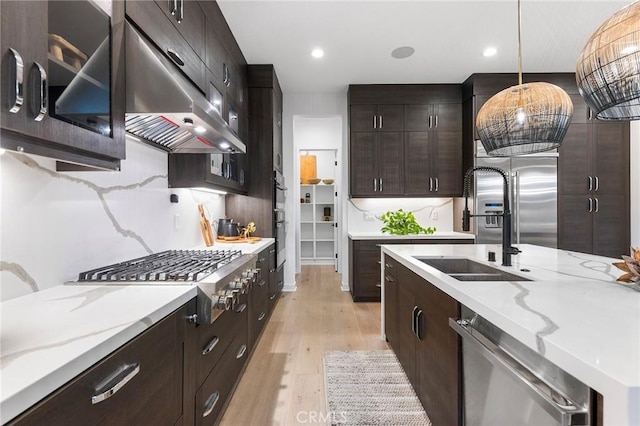 kitchen featuring under cabinet range hood, stainless steel appliances, light wood-style floors, tasteful backsplash, and decorative light fixtures