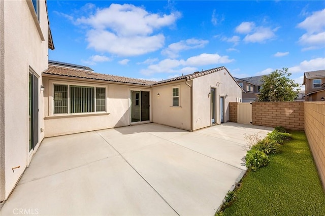 rear view of house featuring solar panels, a tile roof, fence, a patio area, and stucco siding