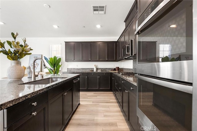 kitchen featuring visible vents, dark stone countertops, wood tiled floor, stainless steel appliances, and a sink