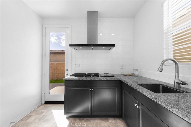 kitchen featuring tasteful backsplash, stone countertops, a sink, dark cabinets, and wall chimney exhaust hood