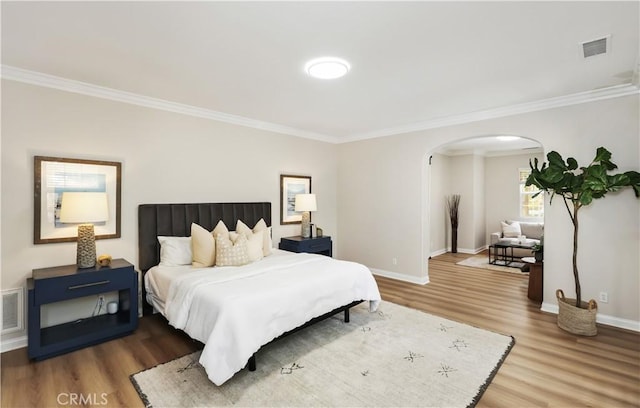 bedroom with arched walkways, ornamental molding, wood finished floors, and baseboards