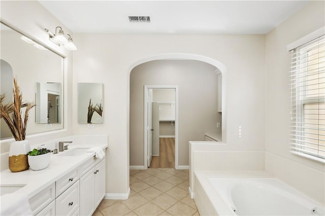 bathroom featuring a garden tub, double vanity, tile patterned flooring, and baseboards