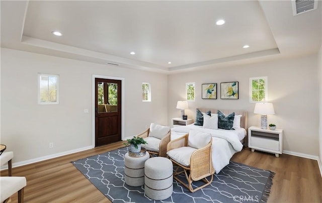 bedroom with a raised ceiling, wood finished floors, multiple windows, and recessed lighting