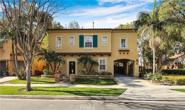 mediterranean / spanish-style home featuring a tile roof, a front yard, concrete driveway, and stucco siding