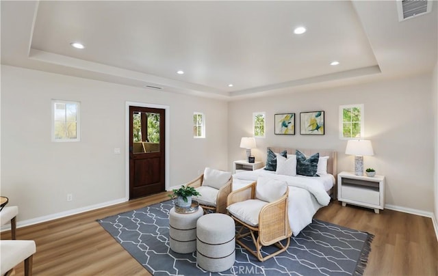 bedroom with a raised ceiling, wood finished floors, multiple windows, and recessed lighting