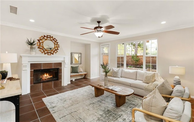 living area featuring a ceiling fan, dark tile patterned floors, baseboards, crown molding, and a tile fireplace