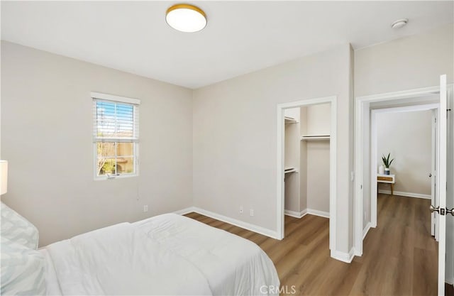 bedroom featuring a closet, a spacious closet, baseboards, and wood finished floors