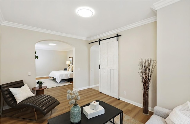 bedroom with a barn door, baseboards, arched walkways, light wood-style flooring, and crown molding